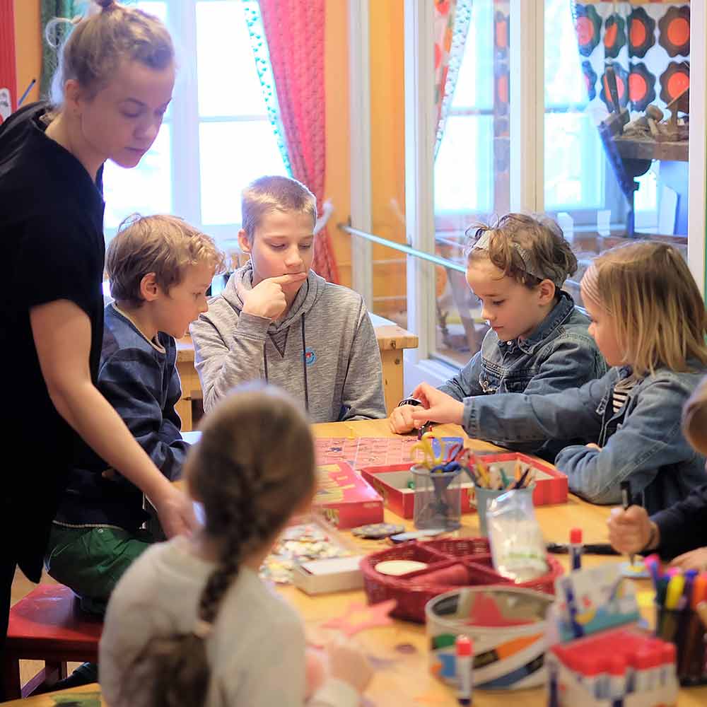 Joukko lapsia on kerääntynyt ison pöydän ääreen askartelemaan.